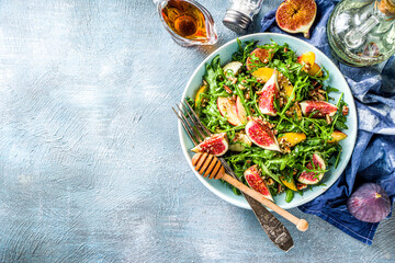 Autumn fig and arugula salad recipe. Whole vegan paleo fruit and vegetable fall salad idea. Homemade salad bowl with figs, arugula, peach and apple slices, nuts and honey. Blue concrete background cop