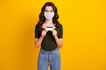 Poster - Portrait of her she nice attractive content wavy-haired girl wear safety mask holding hand bank card mers cov infection prevention stay home isolated bright vivid shine vibrant yellow color background