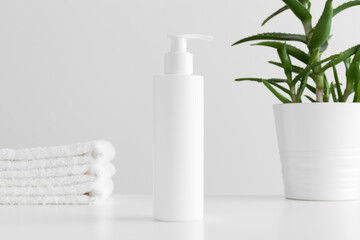 Sticker - White cosmetic shampoo dispenser bottle mockup with a aloe vera and towels on a white table.