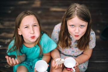 Top view two girlfriends are sitting on a terrace on a sunny summer day eating biscuit and drinking tea. Carefree childhood. Happiness and fun concept. Summer holidays.