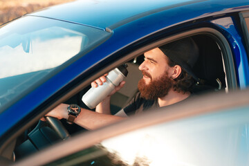 Close up photo of man sitting in car and drinking water from bottle and looking away