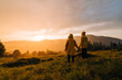 © Ruslan - People in yellow raincoats stand on a meadow in the mountains and watch the beautiful sunset in the rain and shoot with a camera on a tripod. Background. Hikers in the rain at sunset on a hike