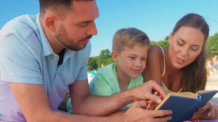 Canvas Print - family, leisure and people concept - happy mother, father and son laying and reading book on summer beach