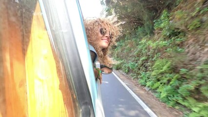 Wall Mural - Concept of travel people and enjoy the wind outside the window of the vehicle car - cheerful enjoyed caucasian woman play with blonde hair and speed outdoor the van smiling and having fun during the t