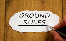 Male Hand Writing 'ground Rules' On White Paper On Wooden Table. Business Concept.