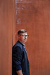 © Pituk - Portrait of young man wearing eyeglasses and leaning against brick wall outdoors.