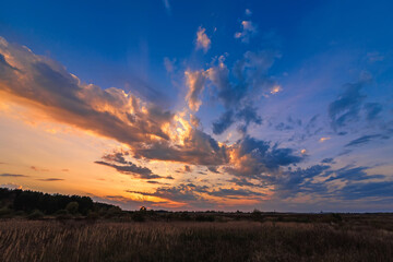 Wall Mural - orange blue sunset with sun rays through the clouds in the sky in the field in the evening