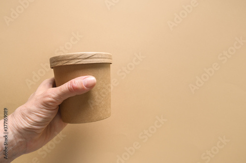 Disposable cardboard soup cup in womans hand on brown background. Ecological individual package.