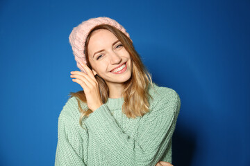 Sticker - Happy young woman wearing warm sweater and knitted hat on blue background