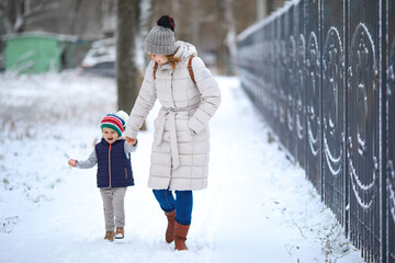 a mother with two young daughter walks in a snow-covered Park. winter walks with children. hardening. happy family.