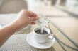 human hand with white sugar packet and pouring in hot black coffee , in soft focus