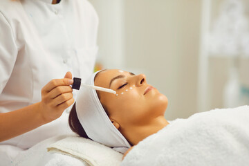 Female beautician applies moisturizing gel on the skin of a young girl at the spa.