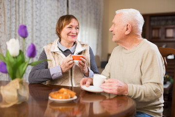 Wall Mural - Cheerful elderly man and woman enjoying conversation over cup of coffee at home..