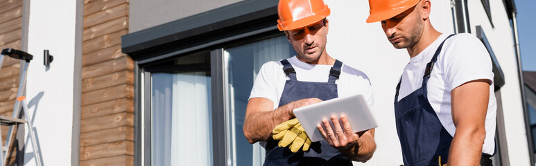 Wall Mural - Horizontal image of workmen in hardhats and uniform using digital tablet near house