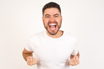 Wall Mural - Close up portrait of stylish handsome caucasian male raising fists up isolated on shine grey background big eyes and wide open mouth.