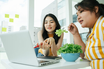 Wall Mural - Asian women eating healthy food for lunch and looking at laptop computer.