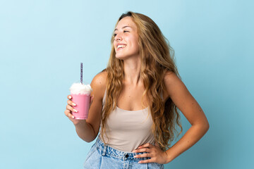 Young woman with strawberry milkshake isolated on blue background posing with arms at hip and smiling