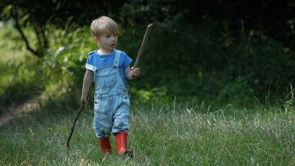 One child walk in green nature and play with wooden stick, free play, happy childhood