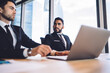 © BullRun - Thoughtful male entrepreneurs in formal clothing sitting at table desk with modern laptop and pondering on productive idea, multiracial colleagues discussing information in office interior