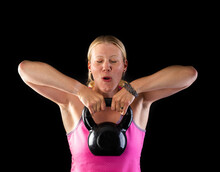 Fitness Woman Wearing Pink Top Lifting Kettlebell Isolated On Black Background