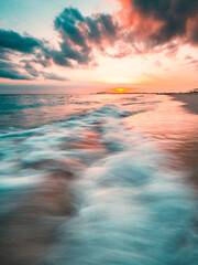 Wall Mural - Ocean sunset, slow shutter, waves washing in over the sand. Strong sunset colors and clouds over the horizon
