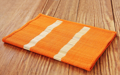 Orange bamboo placemat folded on wooden table.