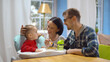 © nimito - Happy parents feeding baby son with healthy porridge sitting at kitchen
