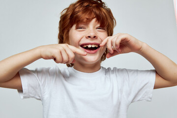 Wall Mural - Cheerful red-haired boy with a wide smile gestures with his hands white t-shirt 