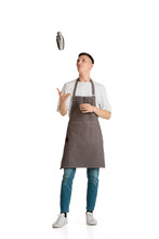 Shaker. Portrait Of A Young Male Caucasian Barista Or Bartender In Brown Apron. Studio White Background, Copyspace. Holding Cocktails, Inviting Guests. Professional Occupation, Drink, Service.