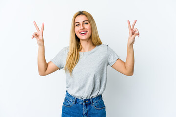 Young blonde woman isolated on white background showing victory sign and smiling broadly.