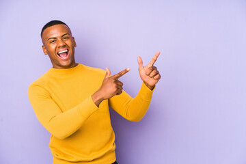 Wall Mural - Young latin man isolated on purple background pointing with forefingers to a copy space, expressing excitement and desire.