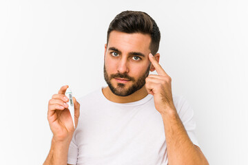 Wall Mural - Young caucasian man holding a thermometer isolated Young caucasian man holding  a pointing his temple with finger, thinking, focused on a task.