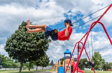 Side View Of Boy On A Swing With Playground In The Background.