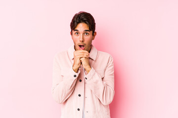 Wall Mural - Young caucasian man posing in a pink background isolated praying for luck, amazed and opening mouth looking to front.