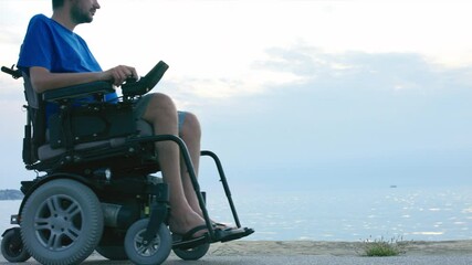 Wall Mural - Man on wheelchair near sea looking at sunset.