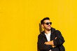© Cavan Images - Young bearded man standing against a yellow wall with crossed arms