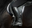 A rider's foot on a black horse close up. A woman's booted foot standing in a black stirrup of horse saddle.