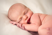 Front View Of Newborn Baby Sleeping With Hands Under His Head