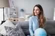 © BestForYou - Smiling woman holding globe sitting on the couch at home. Travel planning.