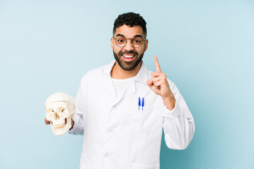 Wall Mural - Young doctor latin man holding a skull isolated having an idea, inspiration concept.