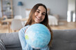 © BestForYou - Smiling woman holding a globe in her hands sitting on the couch.