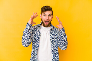 Wall Mural - Young caucasian man isolated on yellow background celebrating a victory or success, he is surprised and shocked.