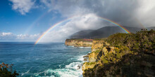 A Double Rainbow In Front Of Dark Clouds Over A Rugged Coastal Cliffs