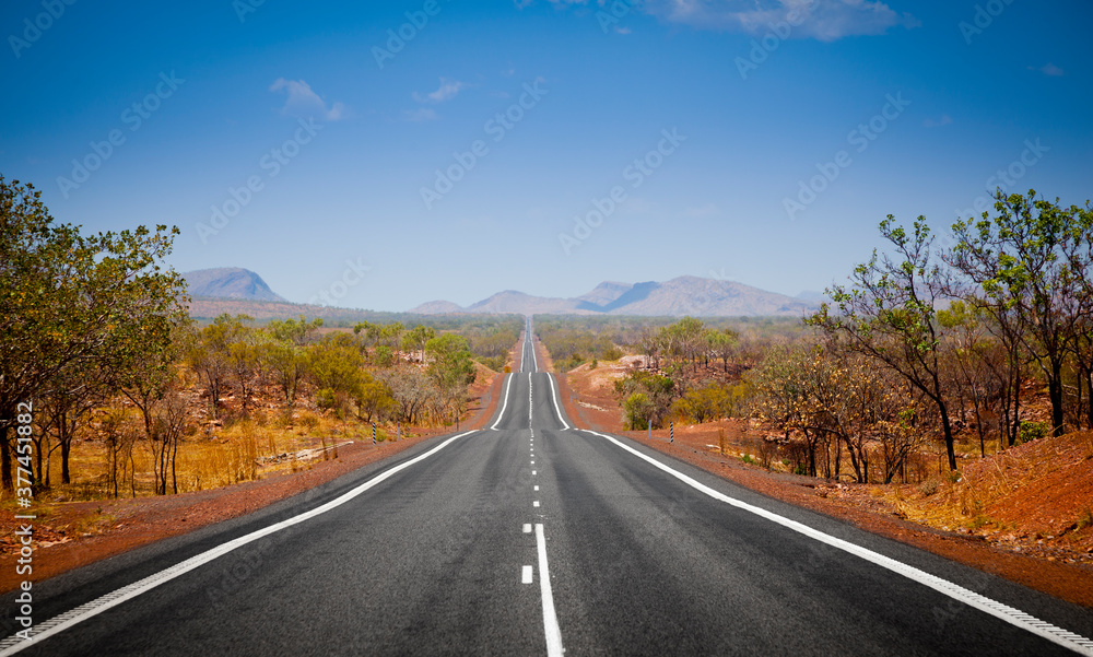 The open road in Kimberly, Western Australia. Straight single lane asphalt road stretching into the distance with mountains in the background. Holiday adventure.
