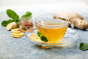 Ginger tea in a glass cup with lemon and mint on light background