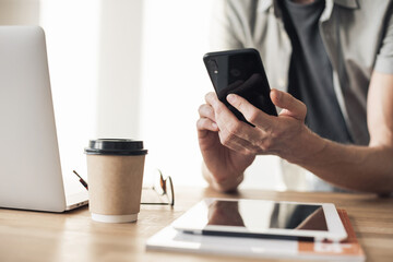 Closeup of young man hands with smart phone and laptop at home, Businessman or student working on computer and texting smartphone at office, Freelance, business, education and technology concept 