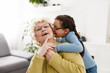 © Angelov - Senior woman hugging granddaughter while sitting on sofa at home