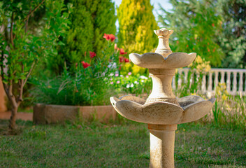 Decorative marble fountain set in a green garden with flowering trees and plants