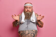 © WHstudio Leushin N - Puzzled bearded man with excess weight, spreads palms and looks confused at camera. Fatso guy faces dilemma how to loose weight. Sweaty overweight European adult male has big tattooed belly.