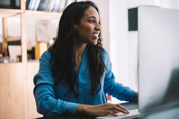 Cheerful black manager typing checking information on monitor at table